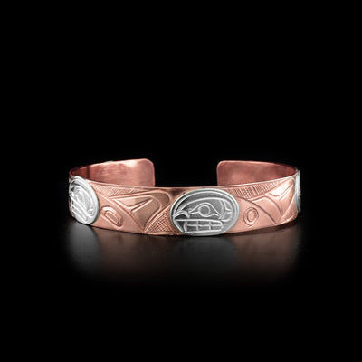 This copper cuff bracelet has three depictions of the Orca carved around its band. The heads of the Orcas are made from sterling silver.