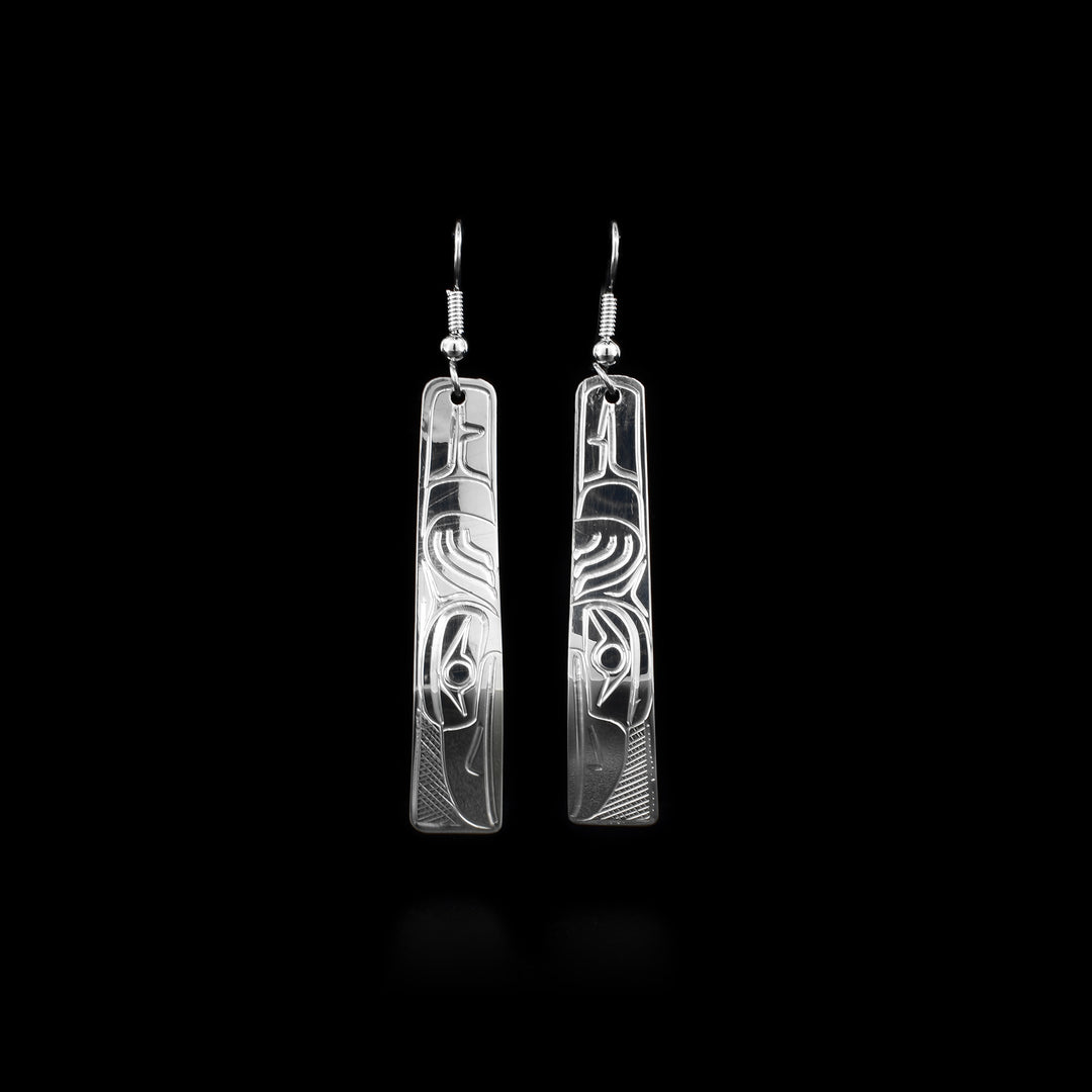 These sterling silver dangle earrings have long, tapered hangs that are slightly curved and rounded at the end. There are depictions of the Raven carved into the surface of the hangs.