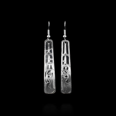 These sterling silver dangle earrings have long, tapered hangs that are slightly curved and rounded at the end. There are depictions of the Thunderbird carved into the surface of the hangs.