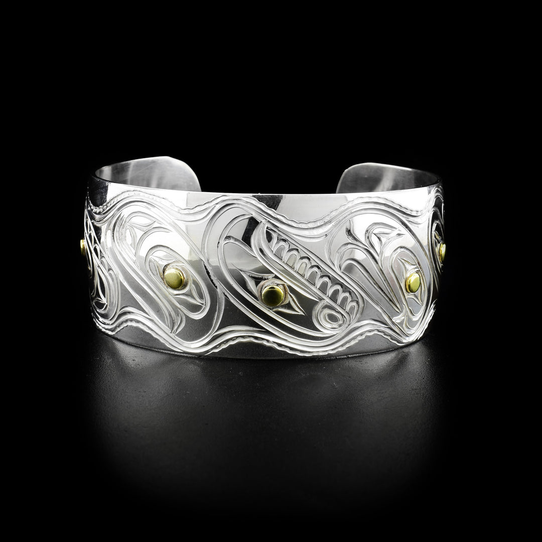 Carved animal heads all the way around cuff. Ravens, orcas, salmons and eagles depicted. Brass pupils, rest of bracelet is sterling silver.