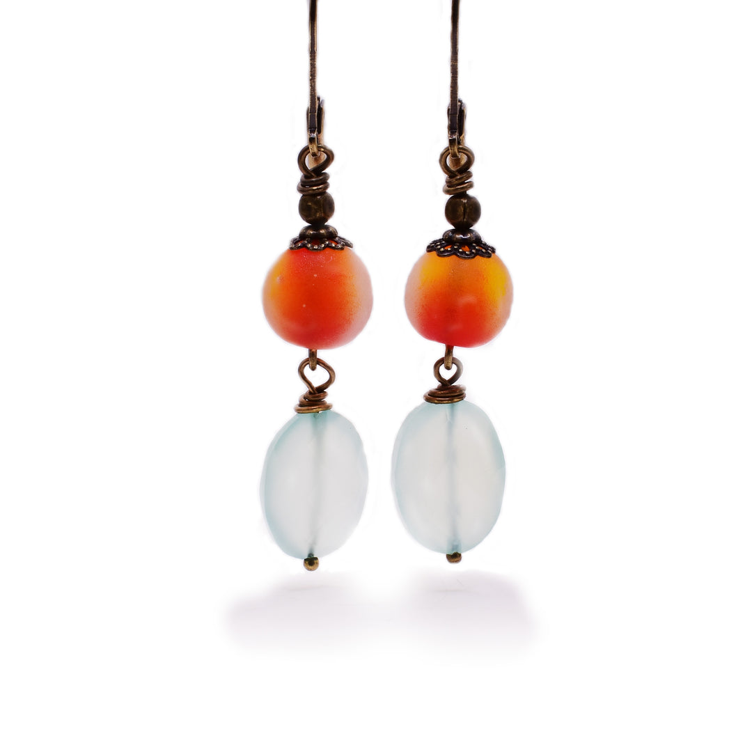 Long dangle earrings with round, translucent orangey handmade lampworked glass beads. Faceted oval blue chalcedony dangles below.