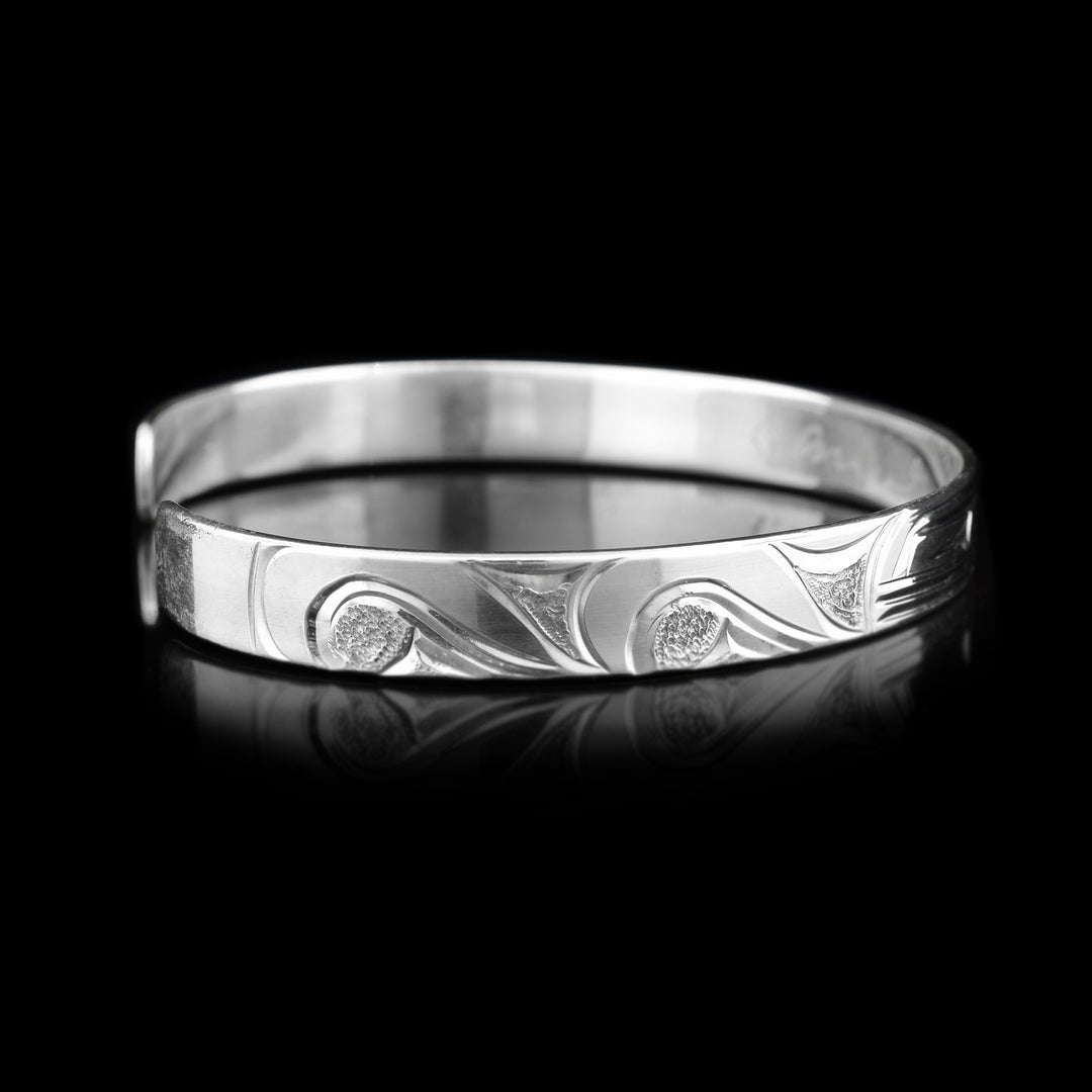 Left side photo of the cuff bracelet depicts carvings representing the waves of the ocean.
