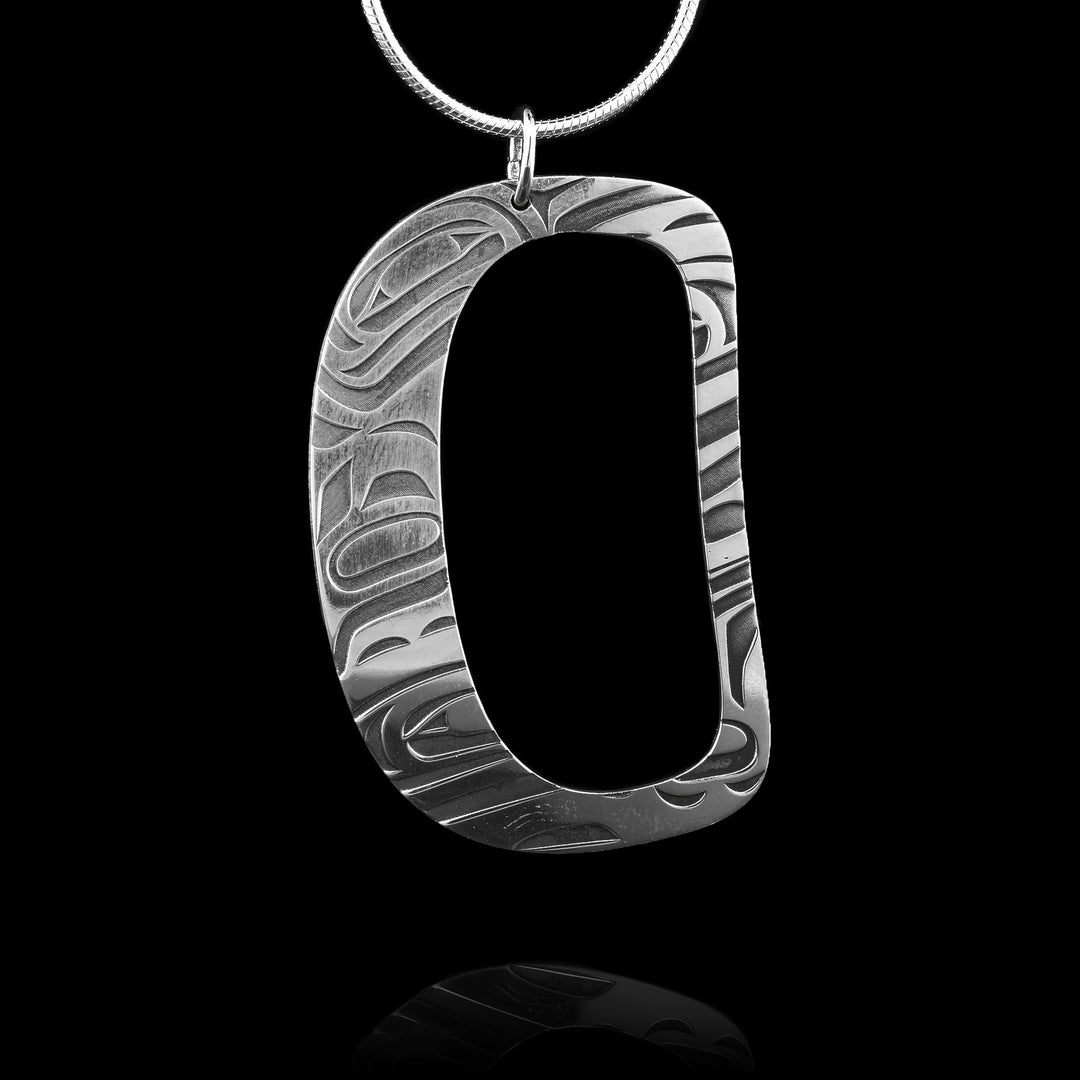 his handcrafted sterling silver pendant features an abstract, asymmetrical oval design, meticulously engraved with the legend of the orca. The center is hollowed out, leaving only the elegant outline adorned with intricate orca.