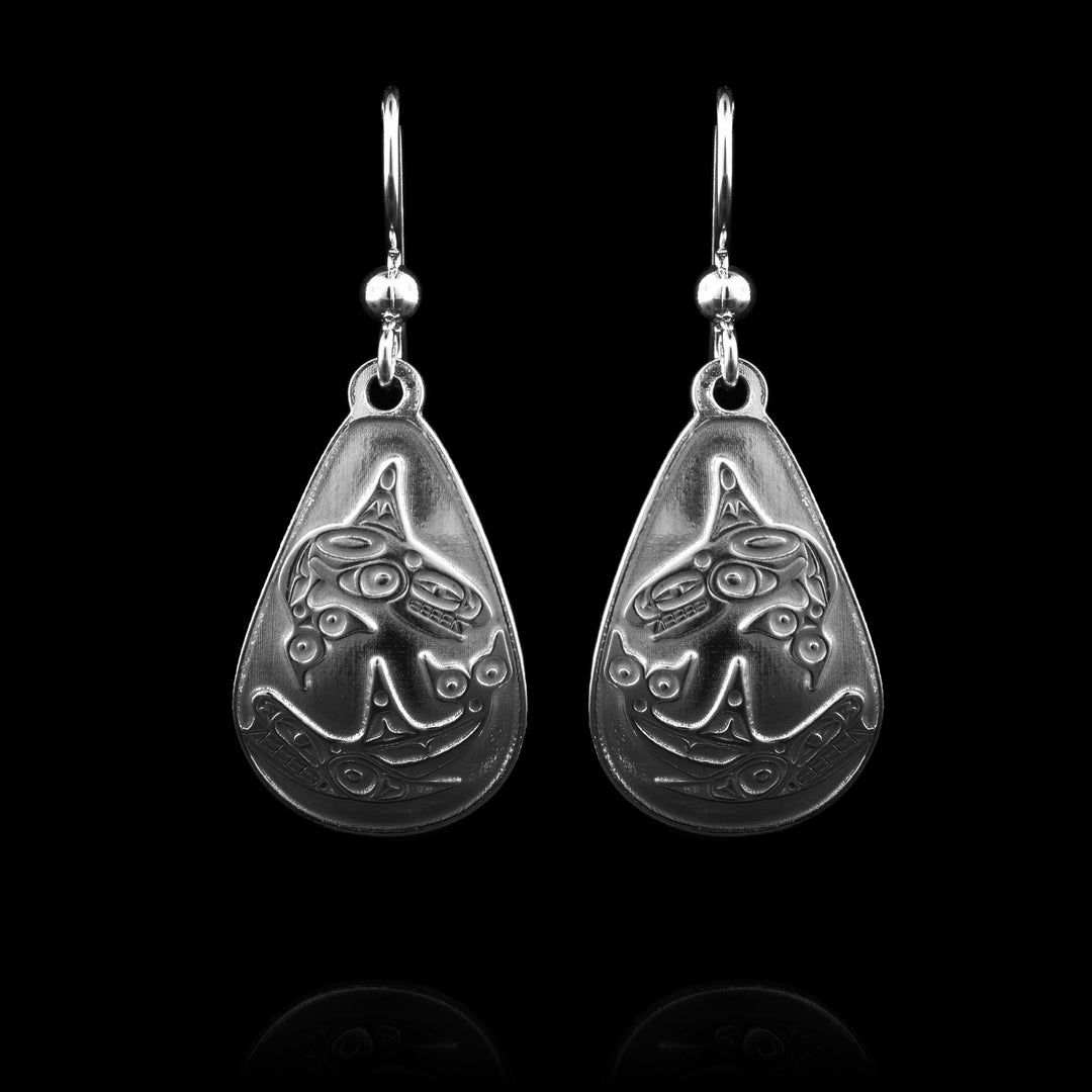 These teardrop dangle earrings feature wide, rounded teardrop-shaped drops crafted from sterling silver. One half of each earring depicts a full-bodied Orca in mid-leap above stylized orca underneath it.