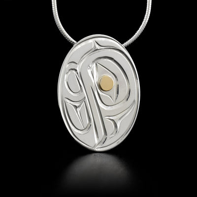 Flat, oval sterling silver pendant featuring eagle with 14K yellow gold in eye. Hidden bail on back.