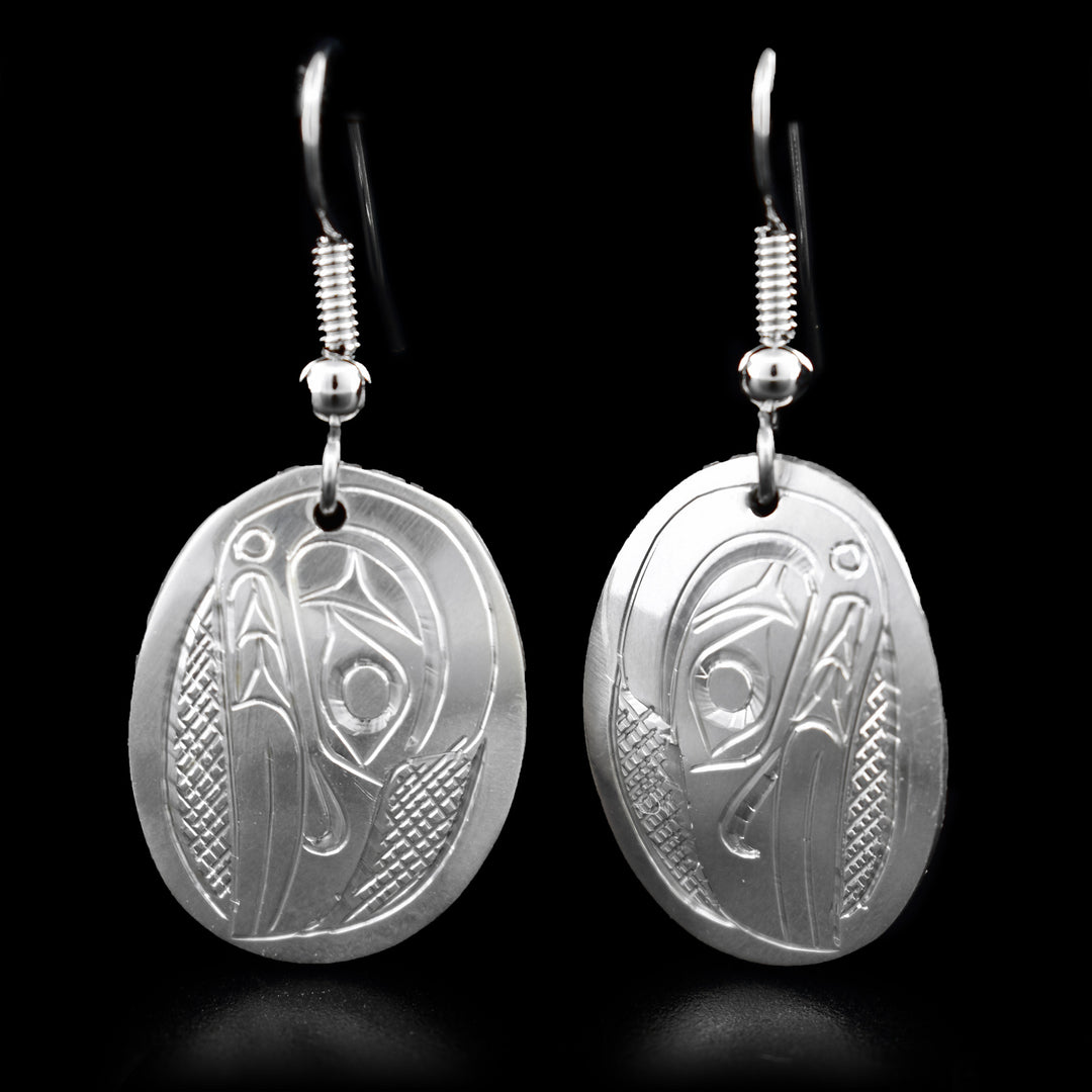 These Raven earrings are made from sterling silver and have oval shaped hangs. There are depictions of the Raven carved into the surface of the hangs.