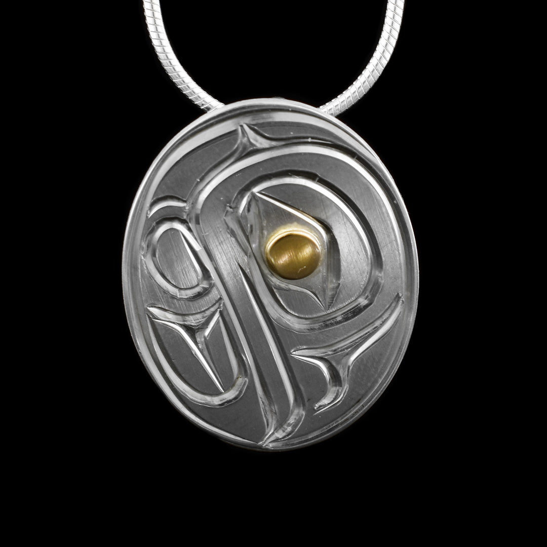 This sterling silver and gold Eagle pendant is oval shaped and there is a depiction of the Eagle carved into the surface of it. The eye of the Eagle is made from 14K gold.