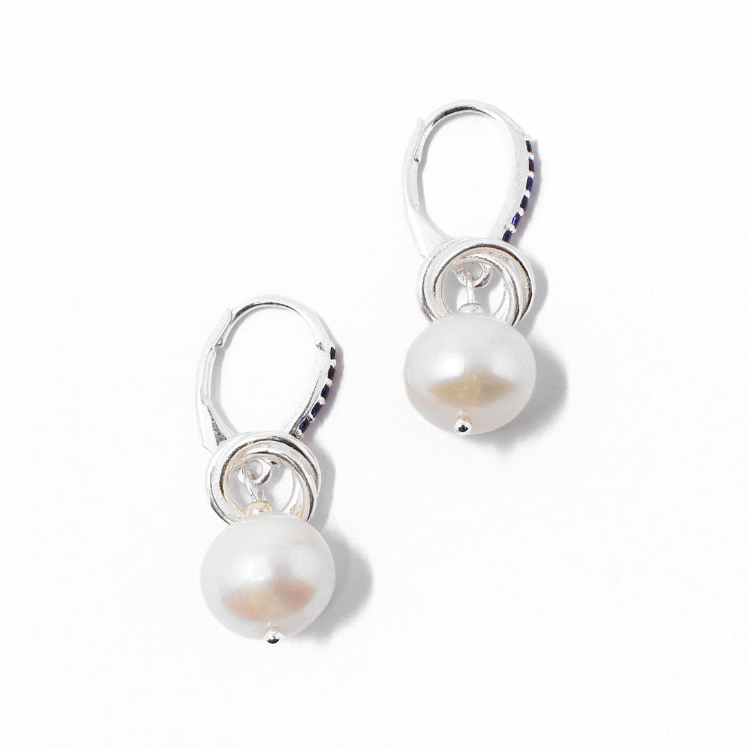 Sterling silver white freshwater pearl dangle earrings with interlocking hoops adornments resting on top. Lever-back hooks are adorned with dark blue cubic zirconia.