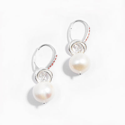 Sterling silver white freshwater pearl dangle earrings with interlocking hoops adornments resting on top. Lever-back hooks are adorned with red cubic zirconia.