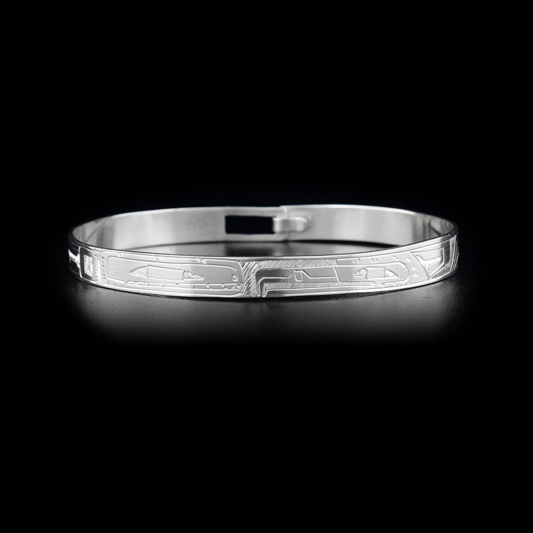 This Orca and Eagle bracelet bangle is made from sterling silver and has a thin band with a clasp in the back. There are carvings on the surface of the band that depict the Eagle and the Orca facing each other. 