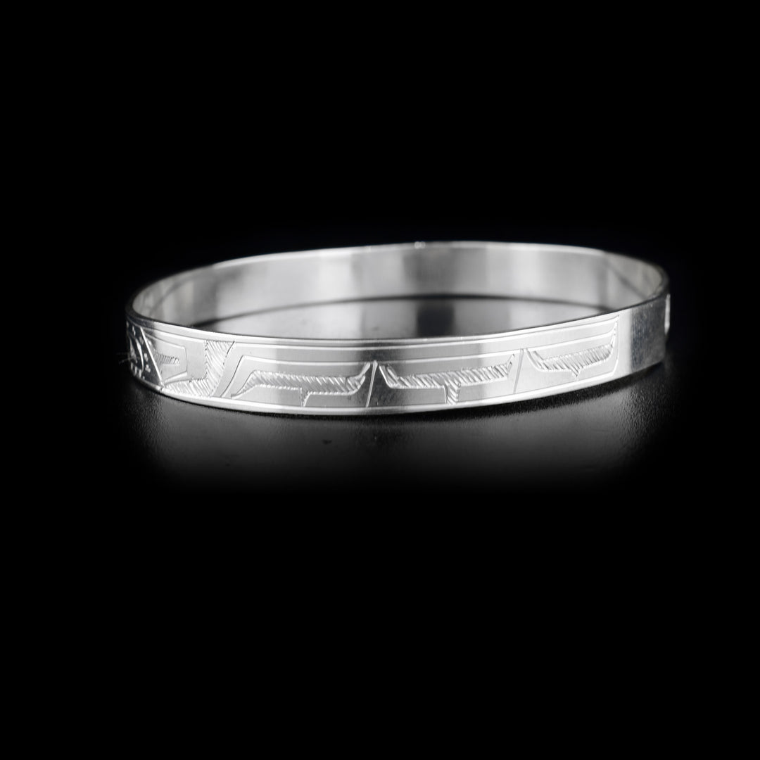 This Orca and Eagle bracelet bangle is made from sterling silver and has a thin band with a clasp in the back. There are carvings on the surface of the band that depict the Eagle and the Orca facing each other. 