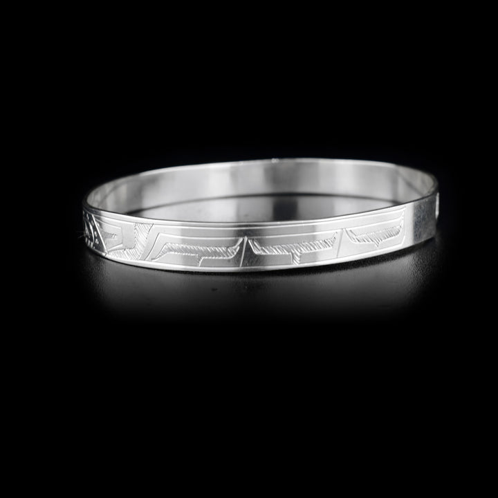 This Orca and Eagle bracelet bangle is made from sterling silver and has a thin band with a clasp in the back. There are carvings on the surface of the band that depict the Eagle and the Orca facing each other. 
