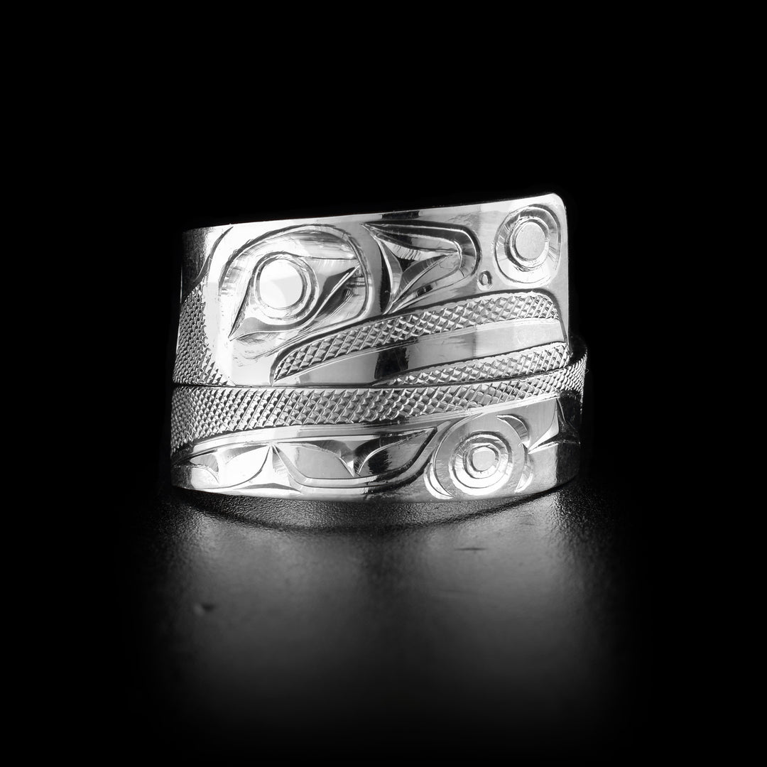 This sterling silver ring has a tapered band that wraps around the finger twice and is made from sterling silver. The head of the Raven is shown at the widest point of the band at a side profile and its details have a slightly 3D appearance. There are cross hatching designs in the background of the scene.