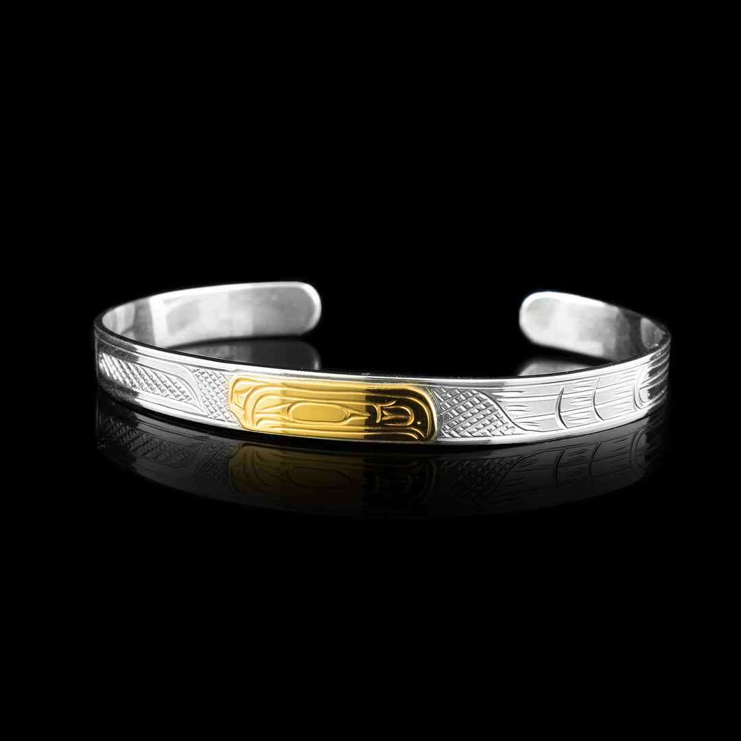 This raven bracelet depicts the head of a raven made from yellow gold in the center of the bracelet facing the right. The background behind the head is cross-hatched. The carvings on the left side depict the wing of the raven.