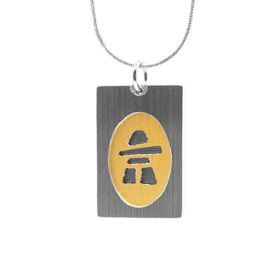 Brushed and anodized aluminum pendant. Rectangular frame and inukshuk done in silver colour. Background of inukshuk is gold colour and oval shaped.
