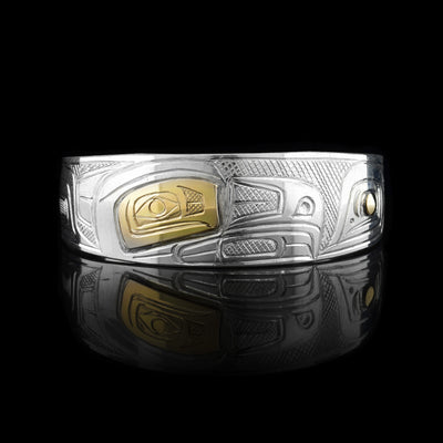 This Salmon and Eagle bracelet cuff is made from sterling silver, 14k gold and has a single, tapered band with a gap in the back. There is a depiction of the Eagle and the Salmon carved into the band. The eyes of the legends are made with gold studs.