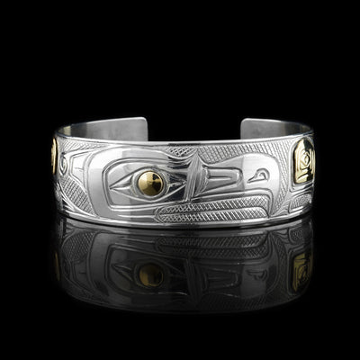 This Thunderbird bracelet is made from sterling silver and 14K gold with a wide band that has a gap in the back. There is a depiction of the Thunderbird carved into the surface of the band and there are gold embellishments on the wings and the eye of it.