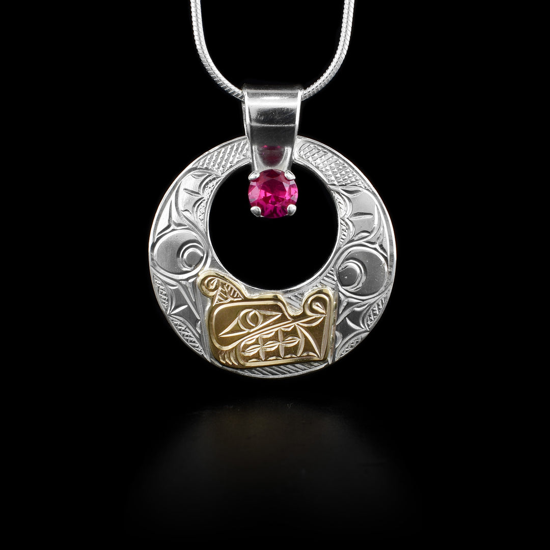 This sterling silver and 14K gold pendant has a circle cutout in the middle with a red gemstone in it. Carved on the pendant is a depiction of a sea serpent. The head of the serpent is 14K gold.
