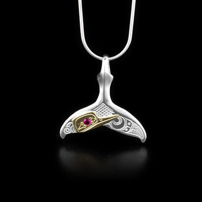 This Hummingbird pendant is made from sterling silver, 14K gold and red lab grown gemstone. The pendant is shaped like a whale tail and has carvings on the surface of it that depict the Hummingbird. The face of the Hummingbird is made from 14K gold and the gem is set into its eye.