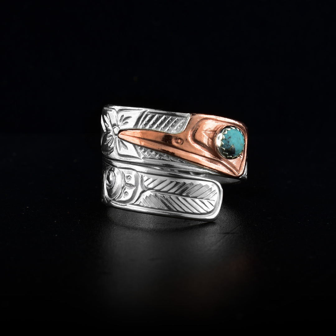 This turquoise wrap ring has a sterling silver band that wraps around the finger twice. The head of the Hummingbird is made from copper and its beak points down the band. There is a small, round turquoise gem embedded o the eye of the Hummingbird. The details of its face are carved into it as well as feather designs down the band with two flowers aswell.