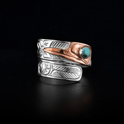 This turquoise wrap ring has a sterling silver band that wraps around the finger twice. The head of the Hummingbird is made from copper and its beak points down the band. There is a small, round turquoise gem embedded o the eye of the Hummingbird. The details of its face are carved into it as well as feather designs down the band with two flowers aswell.