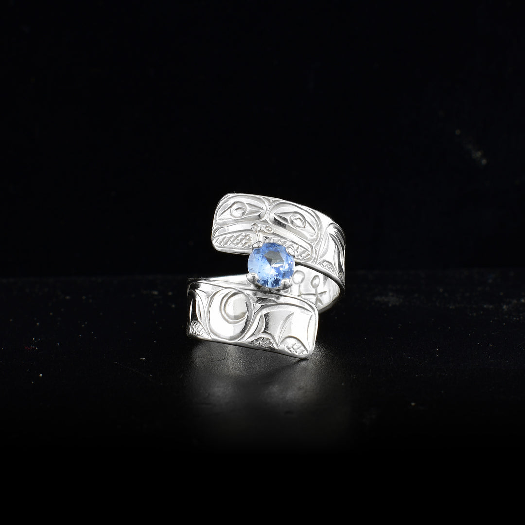 This sky blue gemstone ring is made from sterling silver and has a wrapped band. There is a depiction of a flower and the Frog carved into the surface of it.