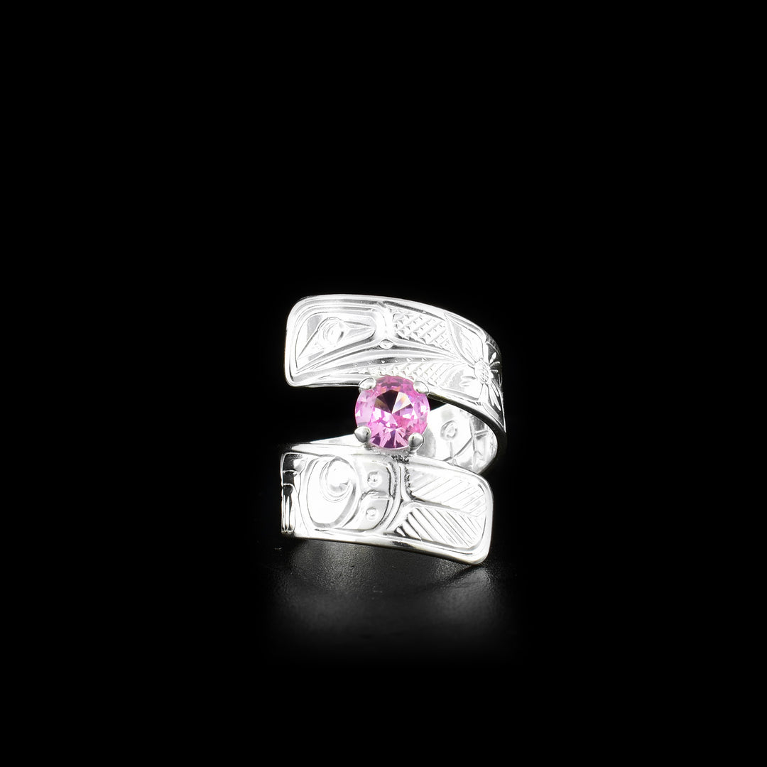 This pink gemstone ring is made from sterling silver and has a wrapped band. There is a depiction of a flower and the Hummingbird carved into the surface of it.