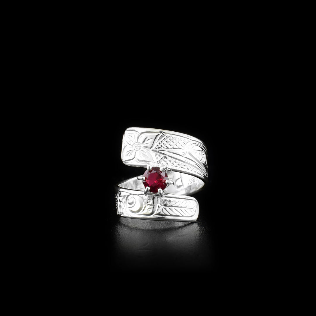 This red gemstone ring is made from sterling silver and has a wrapped, tapered band. There is a depiction of a flower and the Hummingbird carved into the surface of it.