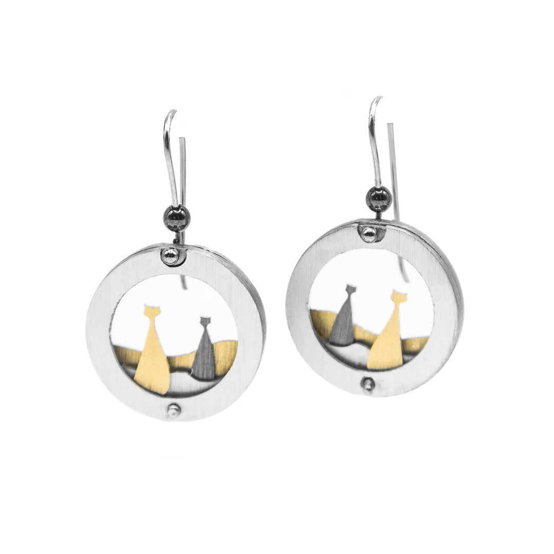 Round silver-coloured frame with grey and gold-coloured cat sitting inside on silver and gold-coloured hills. Brushed and anodized aluminum. Minimalist design.