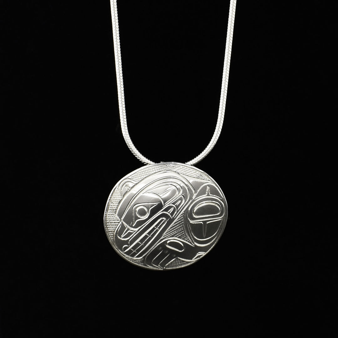 This sterling silver Bear pendant has a domed pendant featuring a side-view of a bear’s arm and face, mouth is open showing teeth. Bear design made of ovoids and lines, background is cross-hatching. 1” diameter. Hidden bail on back.
