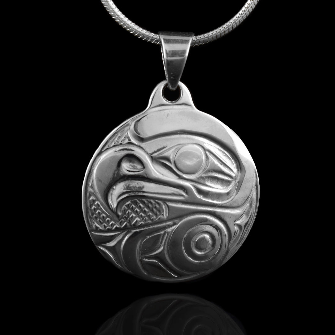 This round pendant is crafted from sterling silver. The eagle’s head is prominently depicted with bold lines and smooth contours, highlighting its sharp beak and keen eye. The background includes fine textured patterns and flowing shapes that add depth and dimension to the design.