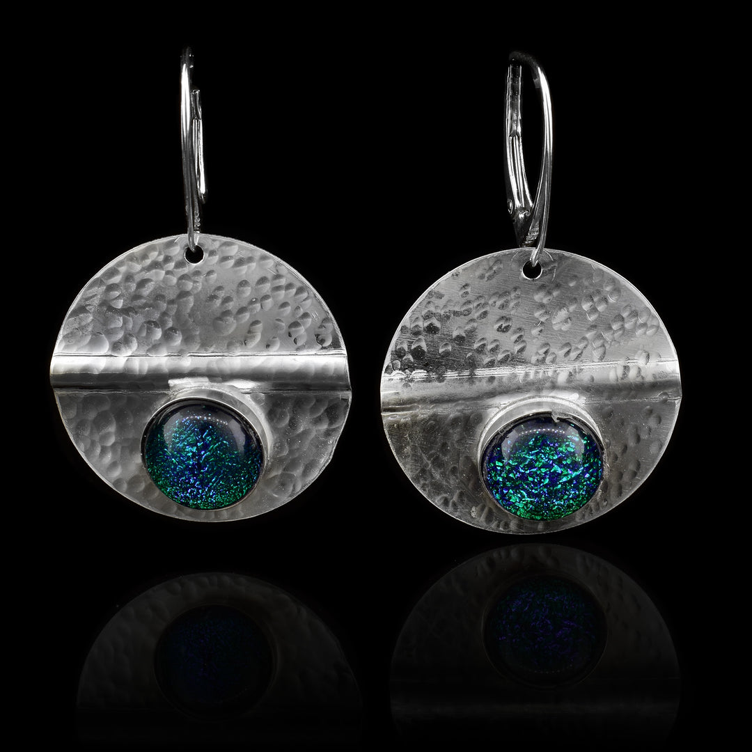 These circle dangle earrings have been made using sterling silver and green colored fused glass beads. The hangs are circle shaped and have dimpled textures on them and a crease running through center of them. The green beads are embossed into the bottom of the hangs.