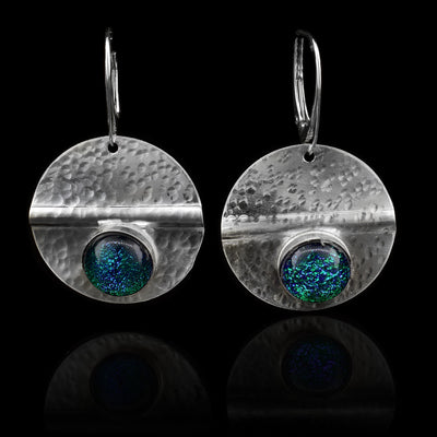 These circle dangle earrings have been made using sterling silver and green/blue colored fused glass beads. The hangs are circle shaped and have dimpled textures on them and a crease running through center of them. The blue beads are embossed into the bottom of the hangs.