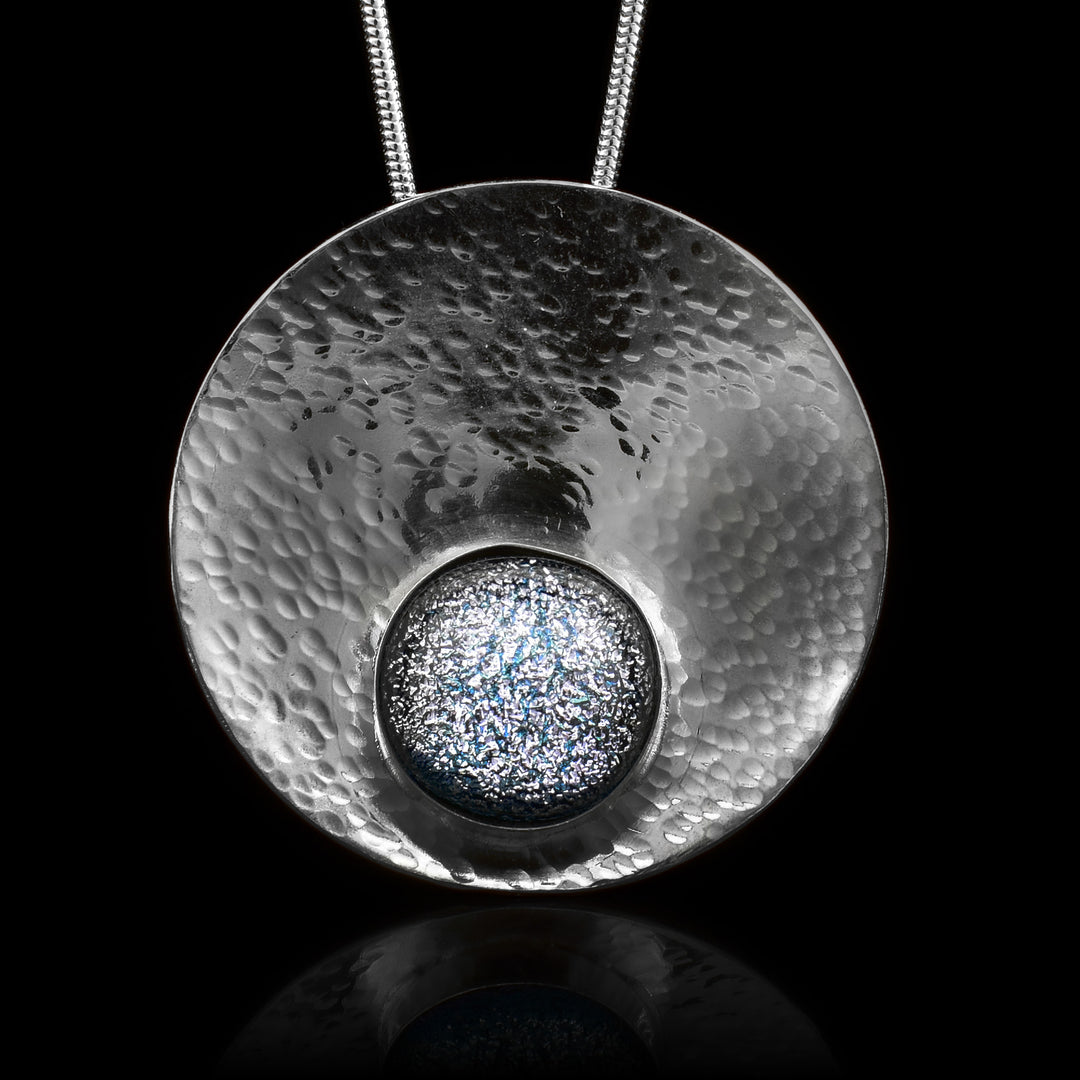 This circle pendant necklace has a circle shaped, sterling silver pendant and is also concaved. There is a denim patterned, fused glass bead that is held in the lower end of the circle pendant.