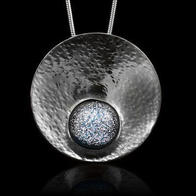This circle pendant necklace has a circle shaped, sterling silver pendant and is also concaved. There is a denim patterned, fused glass bead that is held in the lower end of the circle pendant.