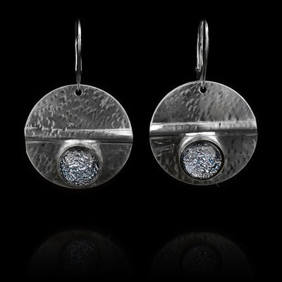 These circle dangle earrings have been made using sterling silver and denim patterned fused glass beads. The hangs are circle shaped and have dimpled textures on them and a crease running through center of them. The denim patterned beads are embossed into the bottom of the hangs.