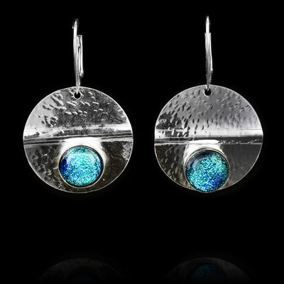 These circle dangle earrings have been made using sterling silver and light blue colored fused glass beads. The hangs are circle shaped and have dimpled textures on them and a crease running through center of them. The light blue beads are embossed into the bottom of the hangs.