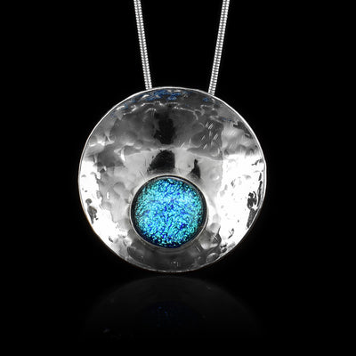 This circle pendant necklace has a circle shaped, sterling silver pendant and is also concaved. There is a light blue, fused glass bead that is held in the lower end of the circle pendant.
