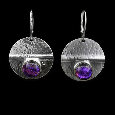 These circle dangle earrings have been made using sterling silver and purple colored fused glass beads. The hangs are circle shaped and have dimpled textures on them and a crease running through center of them. The purple beads are embossed into the bottom of the hangs.