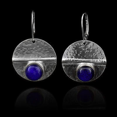 These circle dangle earrings have been made using sterling silver and royal blue colored fused glass beads. The hangs are circle shaped and have dimpled textures on them and a crease running through center of them. The royal blue beads are embossed into the bottom of the hangs.