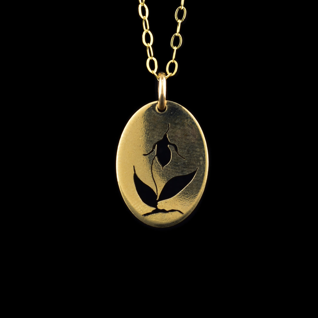 This orchid pendant necklace has an oval shaped pendant dangling from a jump ring and simple chain. All these pieces are made from 14K gold filled material and there is a depiction of the Rocky Mountain orchid cutout into the pendant. There are two leaves at the bottom with a stem reaching up between the leaves and the orchid flowers blooms in the center of the piece.