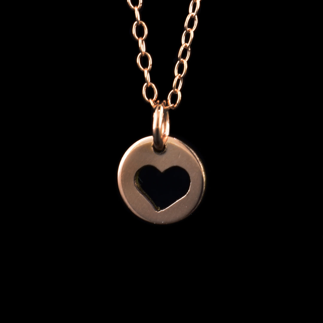 This rose gold heart pendant has a small, circle pendant dangling from a jump ring on a simple chain. These pieces are made from 14K rose gold filled material and there is a heart design cutout into the center of the piece. The heart takes up most of the piece and has somewhat of a hand drawn look to it.