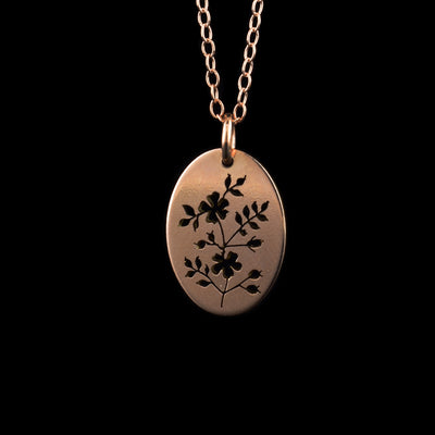 This 14K rose gold necklace and pendant has a dainty, oval shaped pendant dangling from a jump ring and simple chain. All of these pieces are made from rose gold and there is a depiction of a wild rose cutout into the pendant. There are two flowers with leaves extending from the main stem and flower bulbs also.
