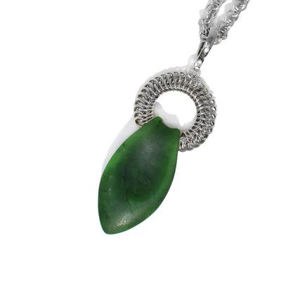 A long leaf-shaped piece of BC jade, with a smooth indent, slopes out of a chainmail ring. Ring is attached to bail. Pendant is 3.5” x 1” including bail.