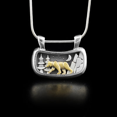 Curved, rectangular oxidized sterling silver forest scene, with night sky, trees and mountains. Side-view of bear in 14K yellow gold walking in middle. Minimalist design. By artist Dennis Kangasniemi.