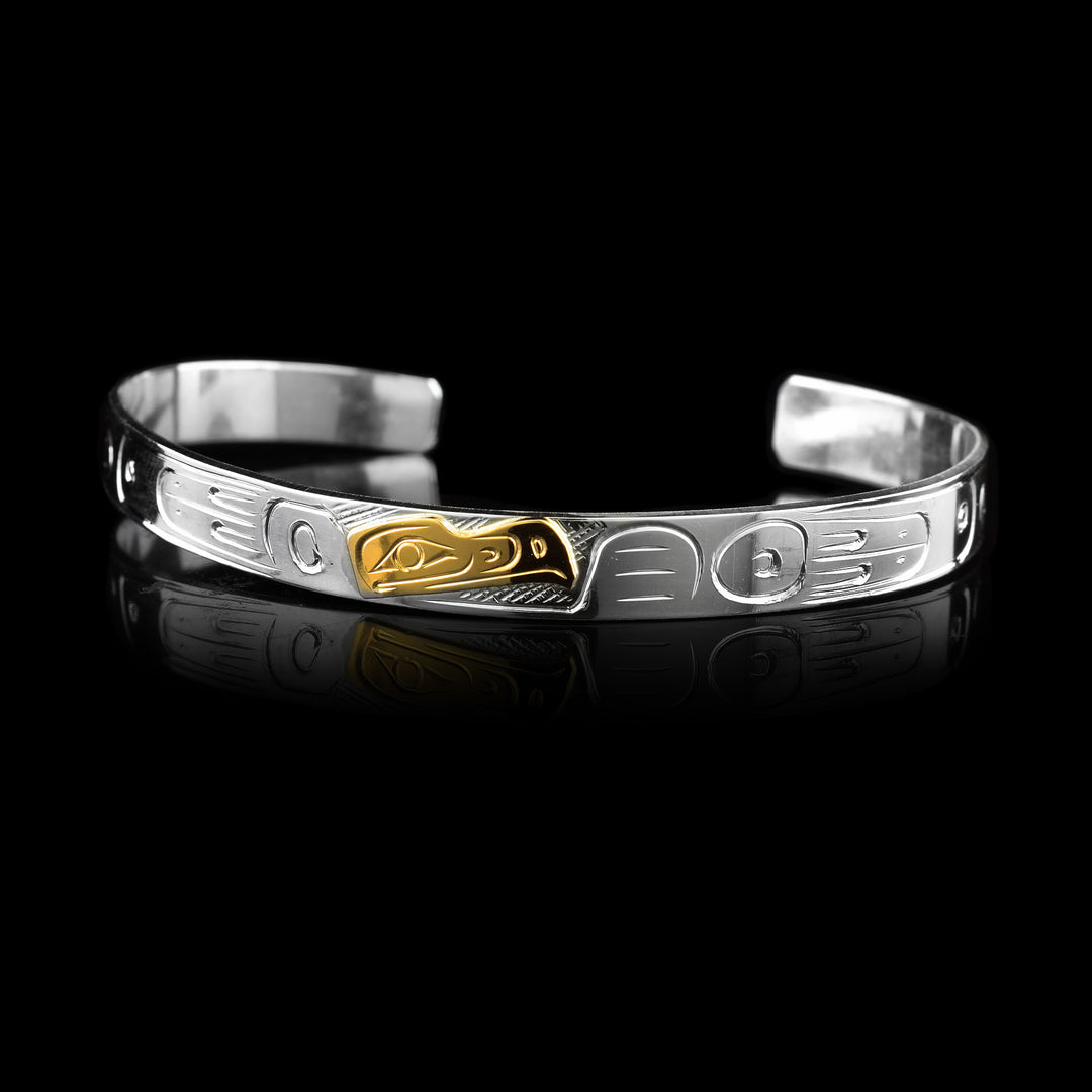 This striking Eagle Cuff Bracelet features a hand-carved sterling silver band adorned with traditional Indigenous markings. At its center, the Eagle Legend is meticulously engraved into 10K gold, creating a beautiful contrast between the metals. This piece serves as a powerful symbol of grace and vision, perfect for any collection.