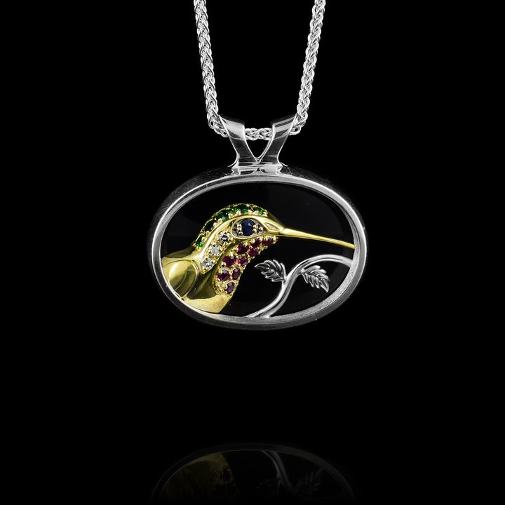 Silver & Gold, Gemstone Hummingbird. The hummingbird is made out of 10k gold and is coloured with ruby's, tsavorite, diamonds and a sapphire for the eye. The other colours resembel the hummingbirds colours. It has a black background and is framed in sterling silver with a small vine meeting the hummingbird in the pendant.