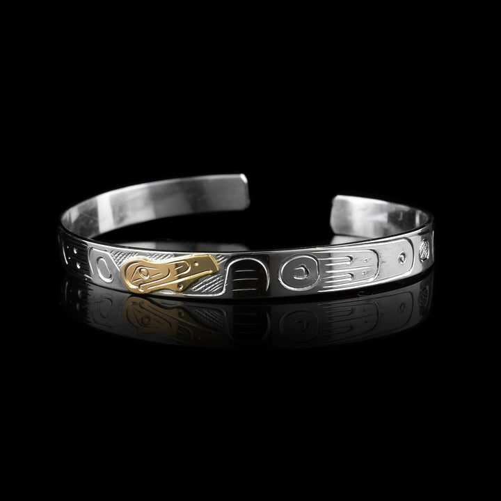 This striking Raven Cuff Bracelet features a hand-carved sterling silver band adorned with traditional Indigenous markings. At its center, the Raven Legend is meticulously engraved into 10K gold