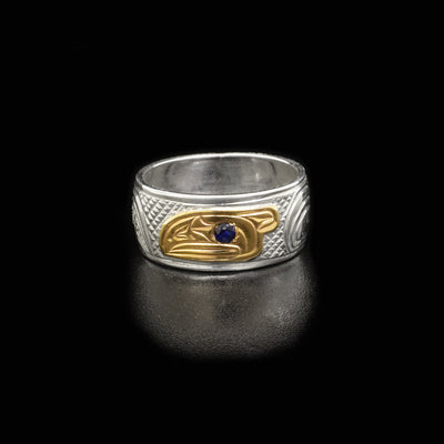 Ring is sterling silver and has side-view of raven’s head in 14K yellow gold in middle. Raven is facing right and has a faceted blue sapphire in eye.