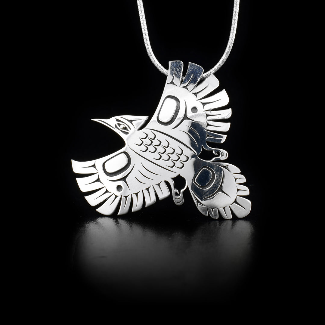 This sterling silver pendant is shaped like and has designs cutout from it that depict a Steller's jay. The eye of the jay is made from 18K gold.